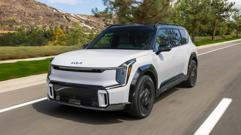 A white Kia EV9 driving on a road in the countryside