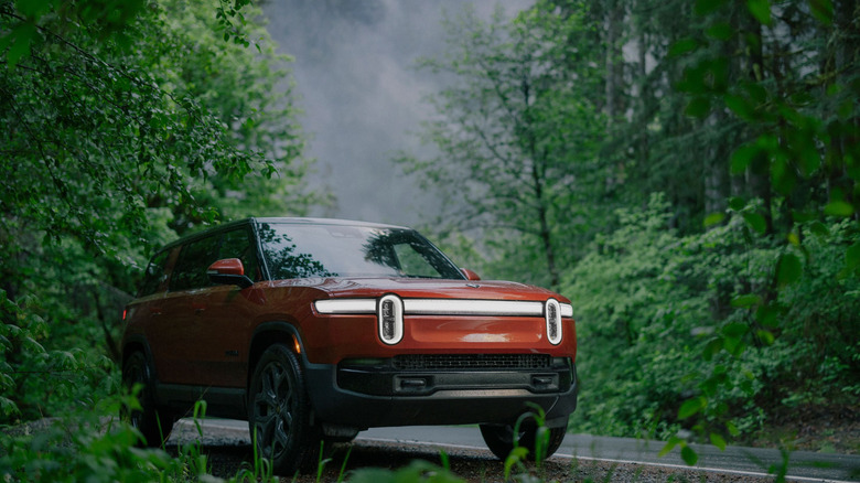 A red Rivian R1S parked at a roadside surrounded by trees