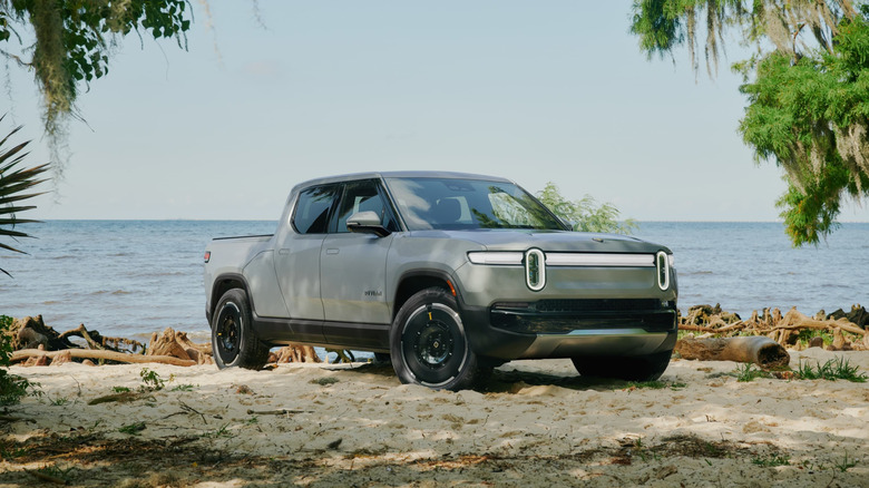 A silver Rivian R1T parked on the sand at a beach