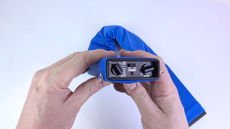 A pair of hands hold one end of a Bone Fone, showing the radio controls.
