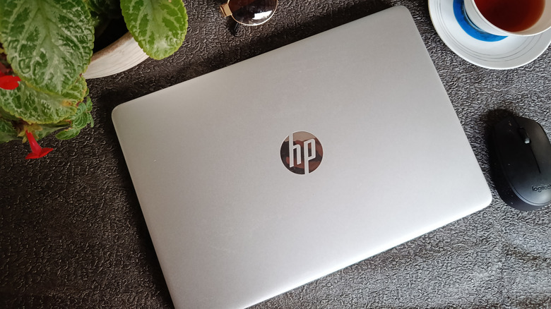 An HP laptop on a gray surface, beside a mouse and a cup of coffee.