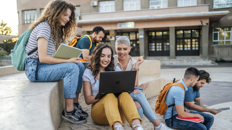 A group of students looking at a laptop while another pair of students are looking at a tablet.