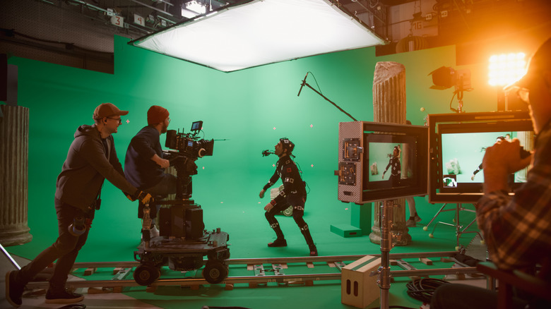 Actors in motion-capture suits film a scene with camera crew and green screen