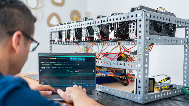 A person uses a laptop to operate a cryptomining rig filled with GPUs.