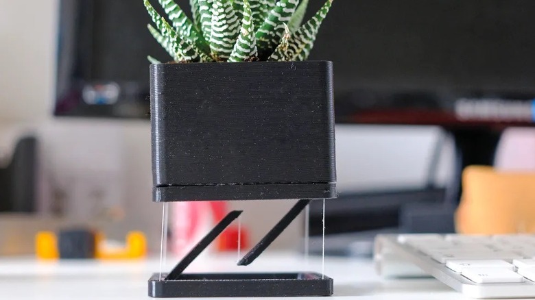 A plant pot appears to float on the desk in a3d printed tensegrity structure