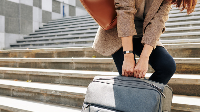 A woman trying to drag a heavy bag up a flight of stairs
