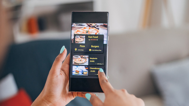A woman holding a phone in her hand browsing food options
