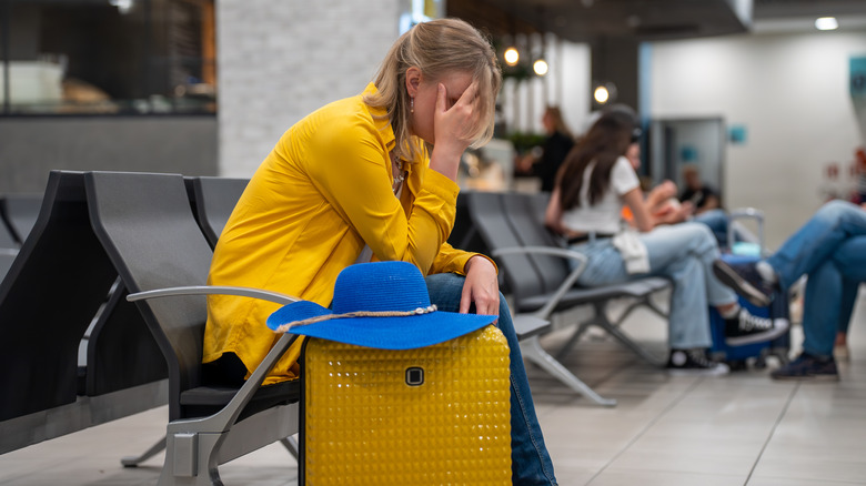 A woman with a suitcase sitting in a chair with her face in her hand