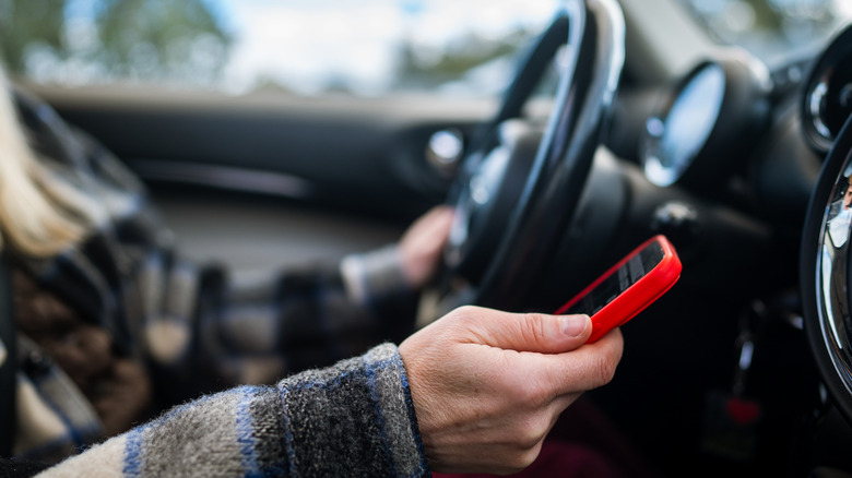 A person holding a phone next to the steering wheel
