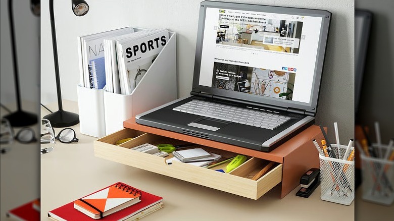 Laptop placed on a stand with a drawer open, alongside other accessories on the desk.