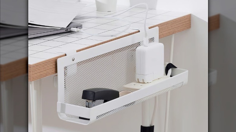 Cable management tray placed on a side of the a desk holding stapler and power cord.