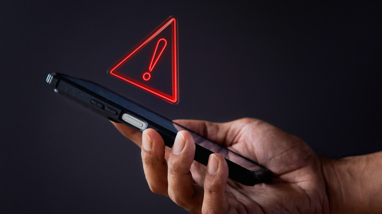 A hand holding an iPhone with a red exclamation mark above the screen.