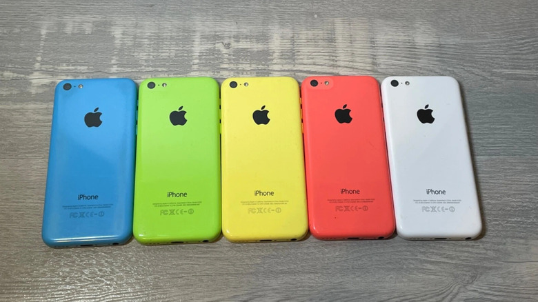 Five iPhone 5c phones lying side by side. From the left, they're colored blue, green, yellow, a coral pink, and white