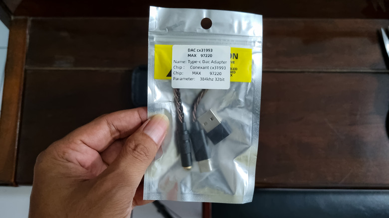 A hand holds a clear bag containing a USB-C DAC.