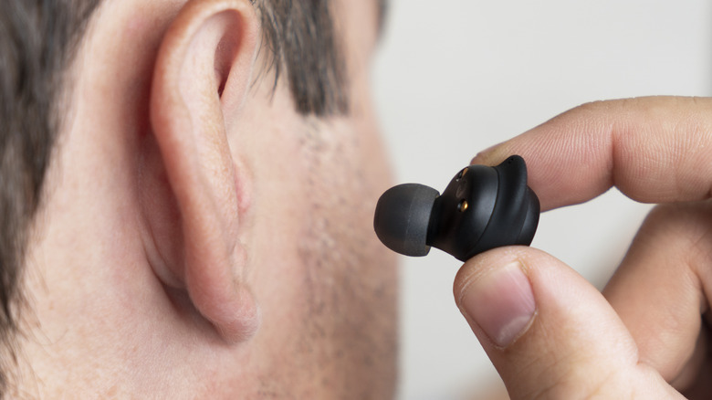 A person putting a wireless earbud in their ear.