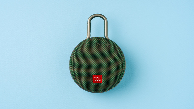 A JBL clip speaker on a solid blue background.