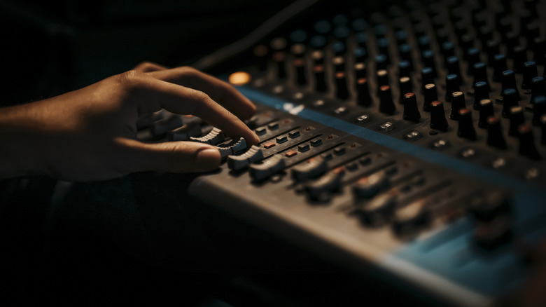 A hand operates the faders on a mixing desk.