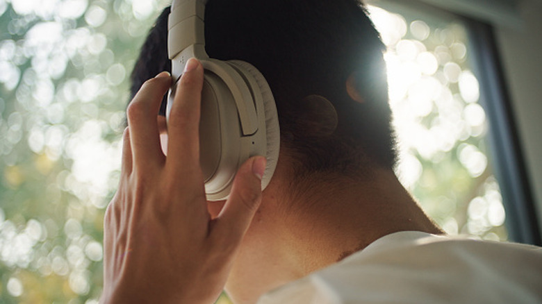 A person adjusts their large over-ear headphones seen from behind.