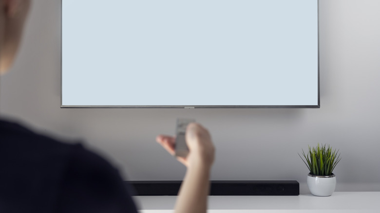 A user configuring holding a remote and pointing it at a TV and soundbar