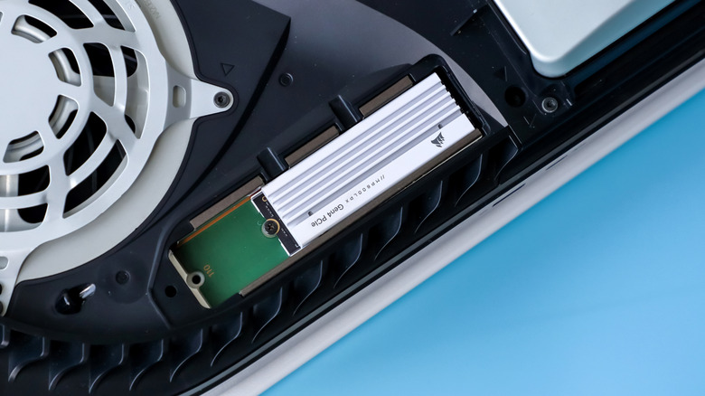 Close-up shot of a white Corsair M.2 SSD installed inside a PlayStation 5 against a light blue background