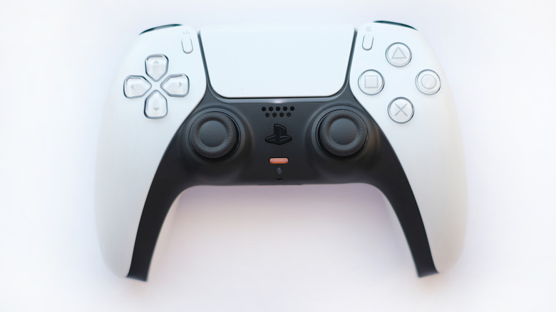 A black and white PlayStation 5 DualSense controller with the red mute button light turned on