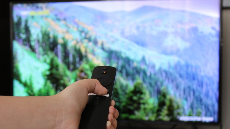 Holding the Fire TV remote as the television shows a screensaver
