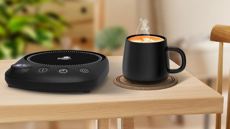 Black mug containing a hot beverage beside a mug warmer