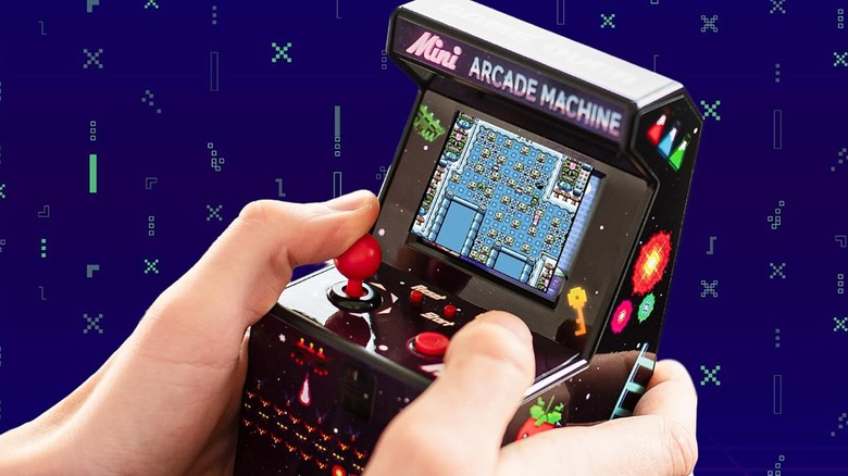Playing a game on a mini arcade machine placed against blue pixelated background.