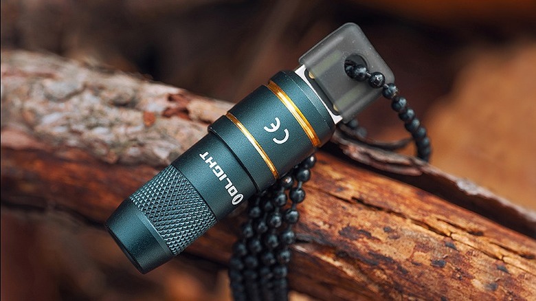 Olight keychain flashlight strapped with beads onto a small wooden log.