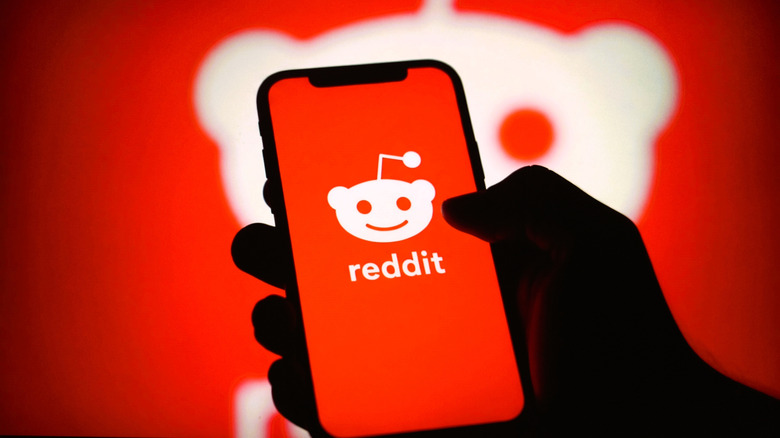 The Reddit logo on a smartphone held in front of a bigger Reddit logo
