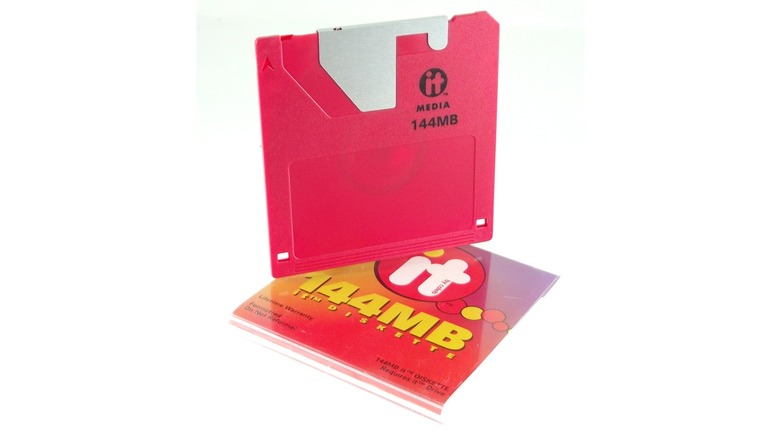 A red 144MB floppy disk standing on top of its cover.