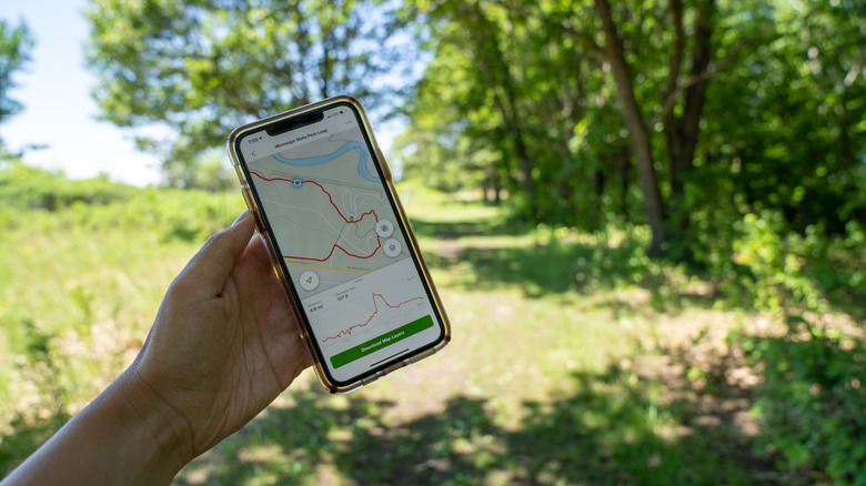 A person holding up an iPhone that displays a hiking map in the Alltrails app