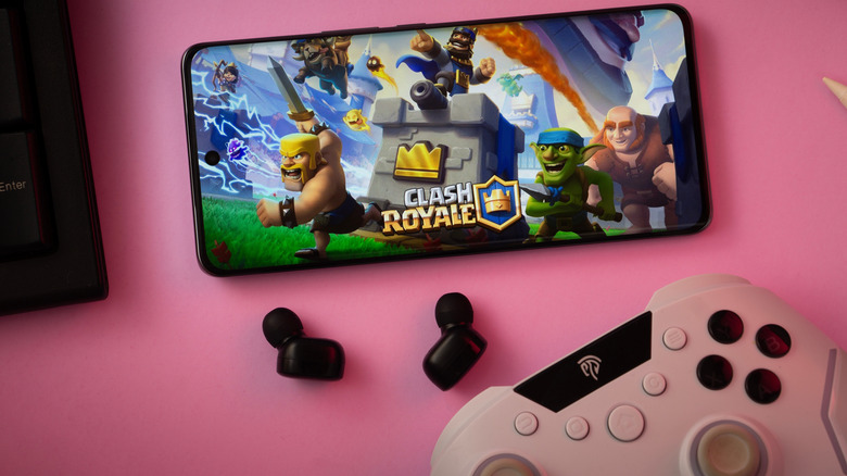 A close-up of a gamepad with the Clash Royale seen on smartphone.