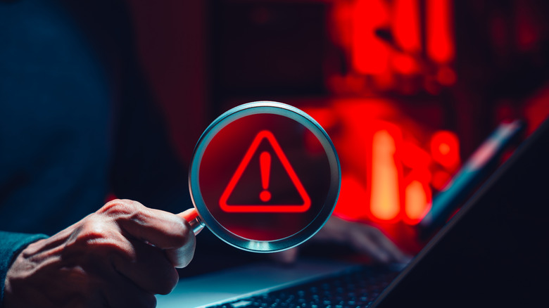 man holding magnifying glass over laptop, concept of malware discovery