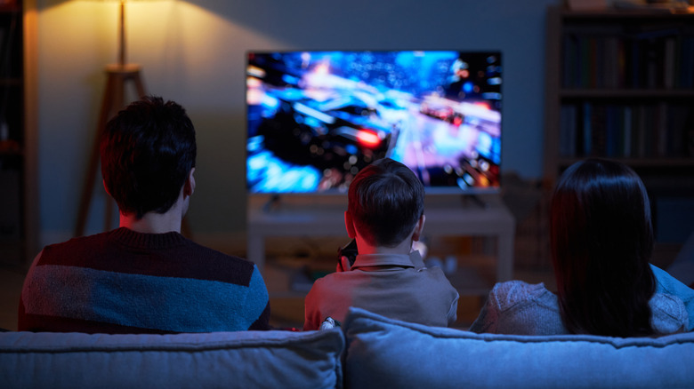 Family sitting on a couch playing a video game on TV.