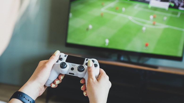 Person holding a controller playing a soccer game on TV.