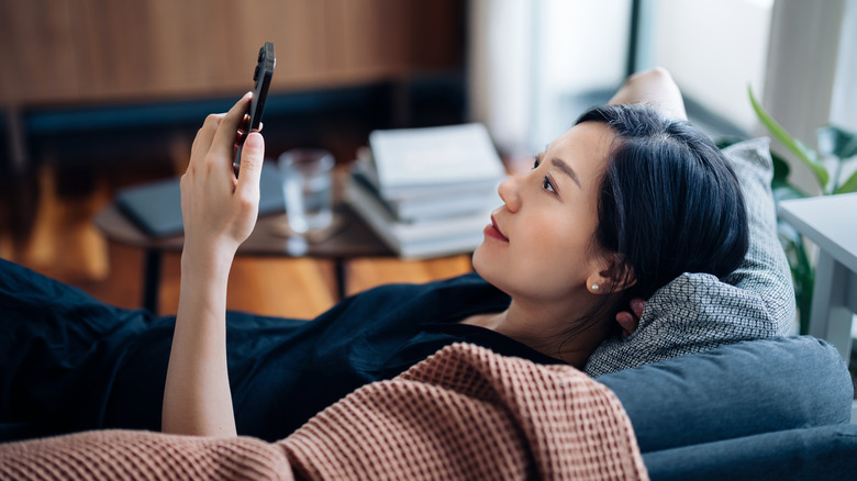 Woman lying back on couch and reading phone