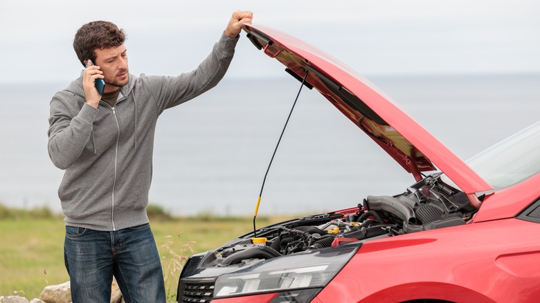 Man standing in front of broken down car with hood open and talking on phone