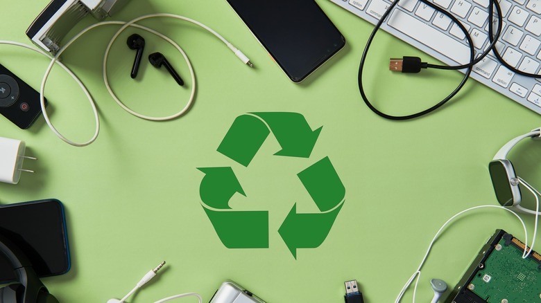 A collection of various electronics and wires surrounding a recycle symbol