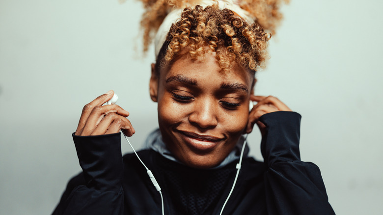A smiling woman with eyes closed is putting on wired earphones