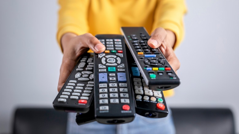 A person holding out several tv remotes in their hands