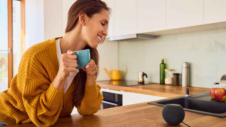 Smiling woman using smart speaker in kitchen while having a coffee
