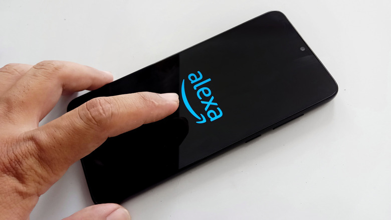 A hand holds a smartphone displaying the Alexa logo