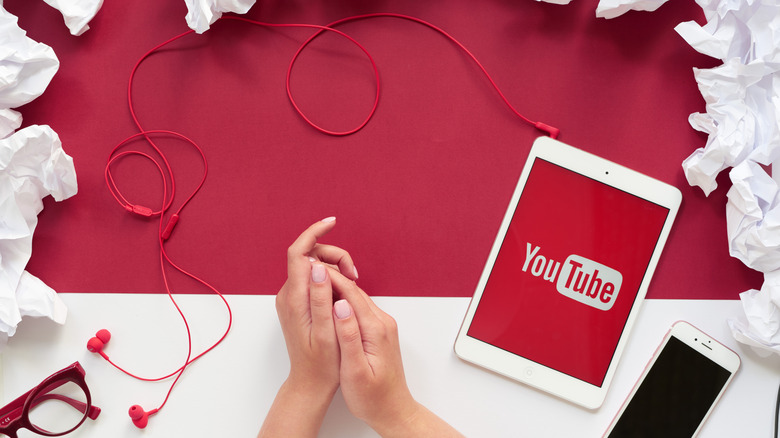 A tablet with the YouTube logo next to a phone with red wired earphones plugged in, placed on a red and white table