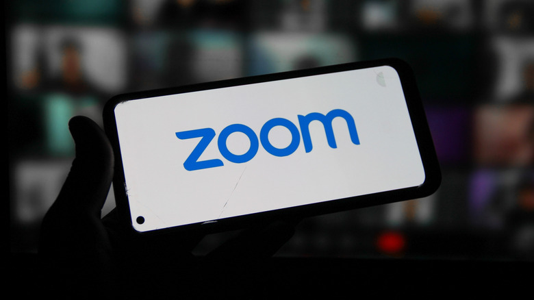 The Zoom logo on a phone in front of a blurred video conference call
