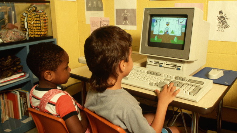 Two children playing a game on a 1990s computer in a classroom