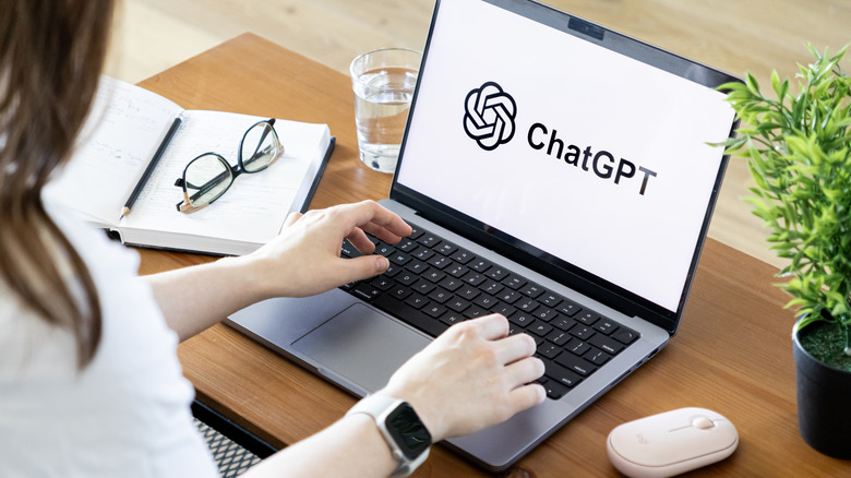An individual sitting at a desk, their hands are on a laptop that's displaying the ChatGPT logo.