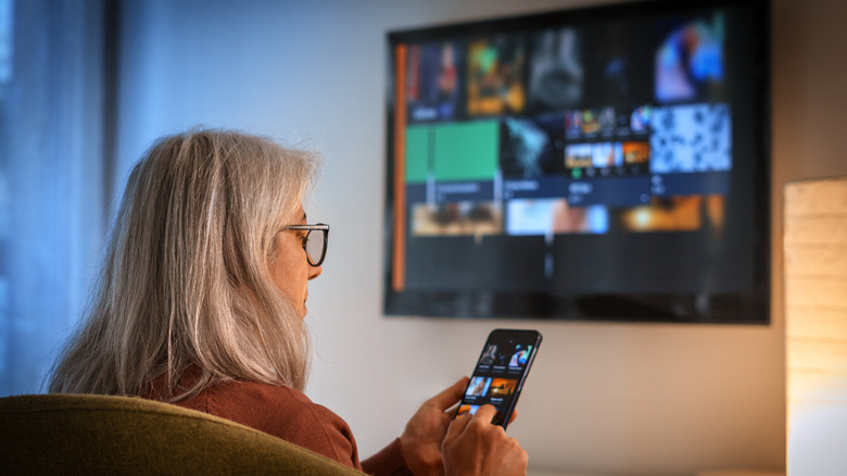 A woman using a smartphone while viewing content on TV