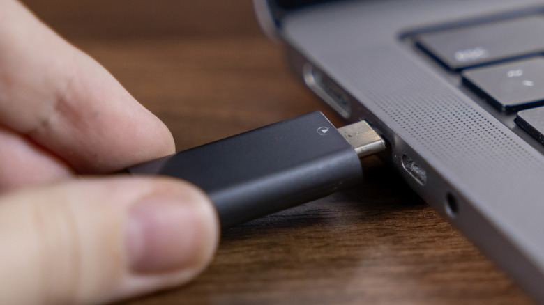 A person inserting a USB flash drive into laptop port