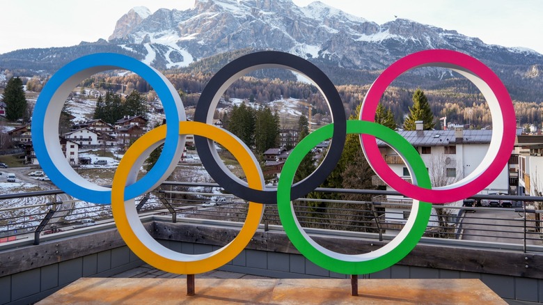 A statue of the five Olympic rings sitting on an outdoor patio in front of a mountain
